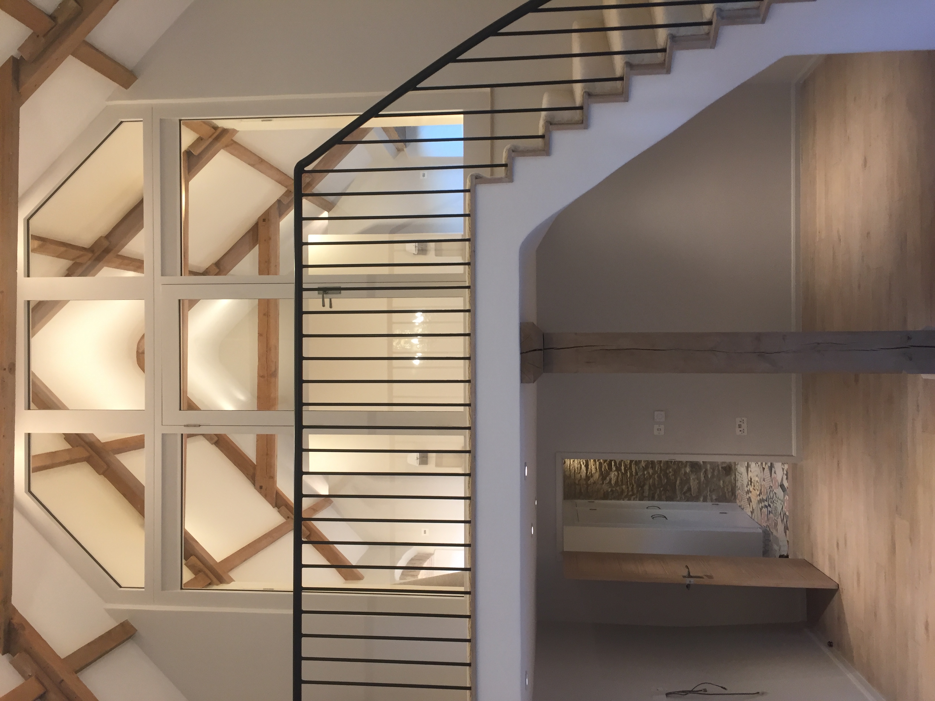 Bespoke curved staircase with wrought-iron balustrade and full-height glazed gallery above
