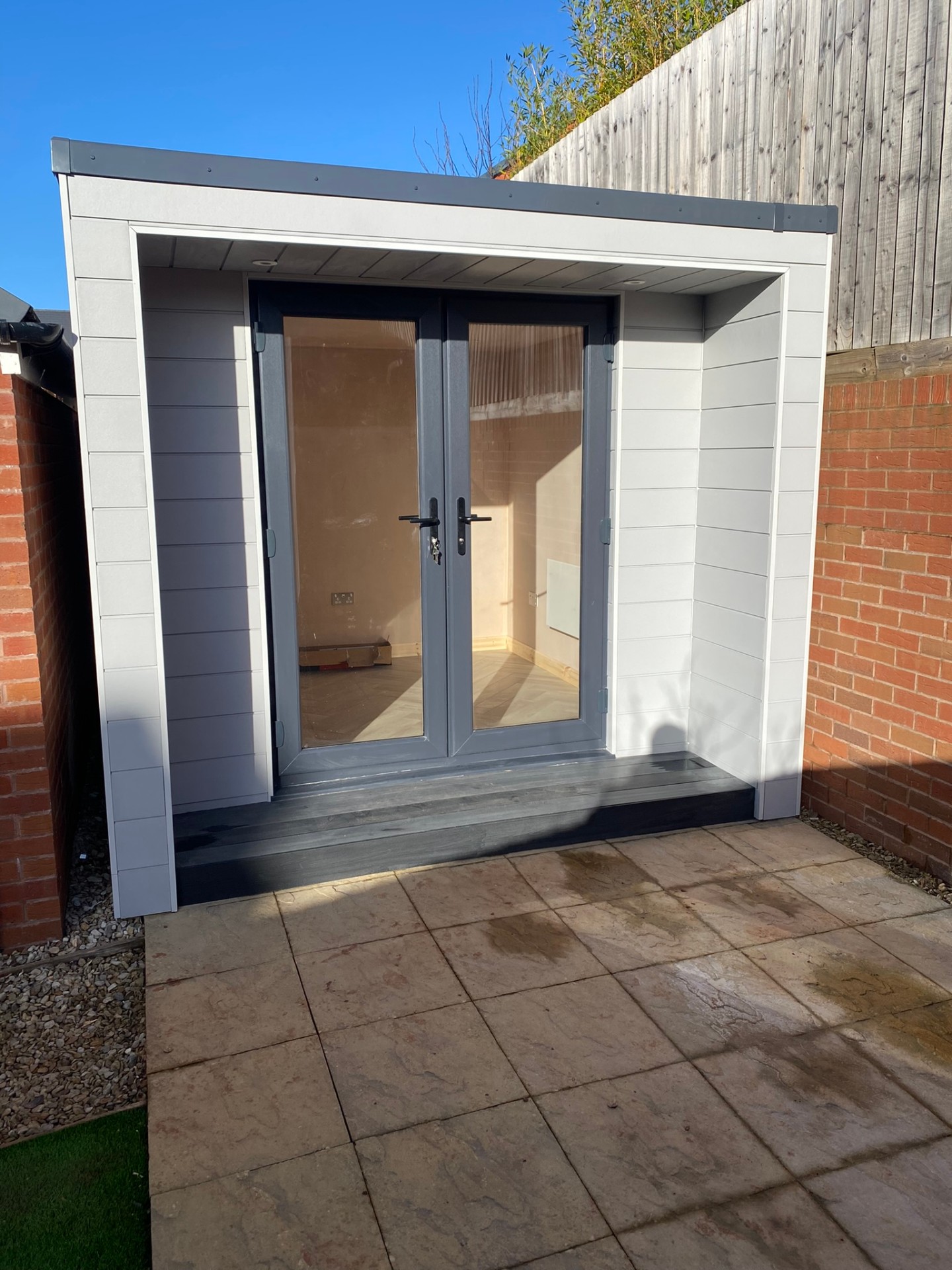 Compact contemporary garden office with grey French doors and paved patio