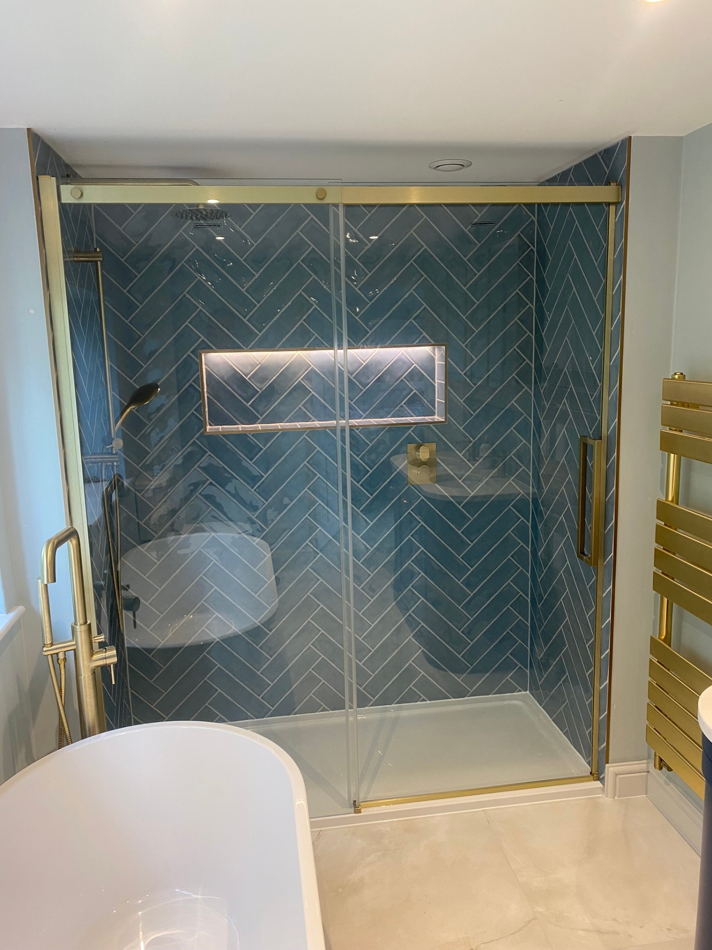 Walk-in shower with teal herringbone tiles and brushed brass fittings