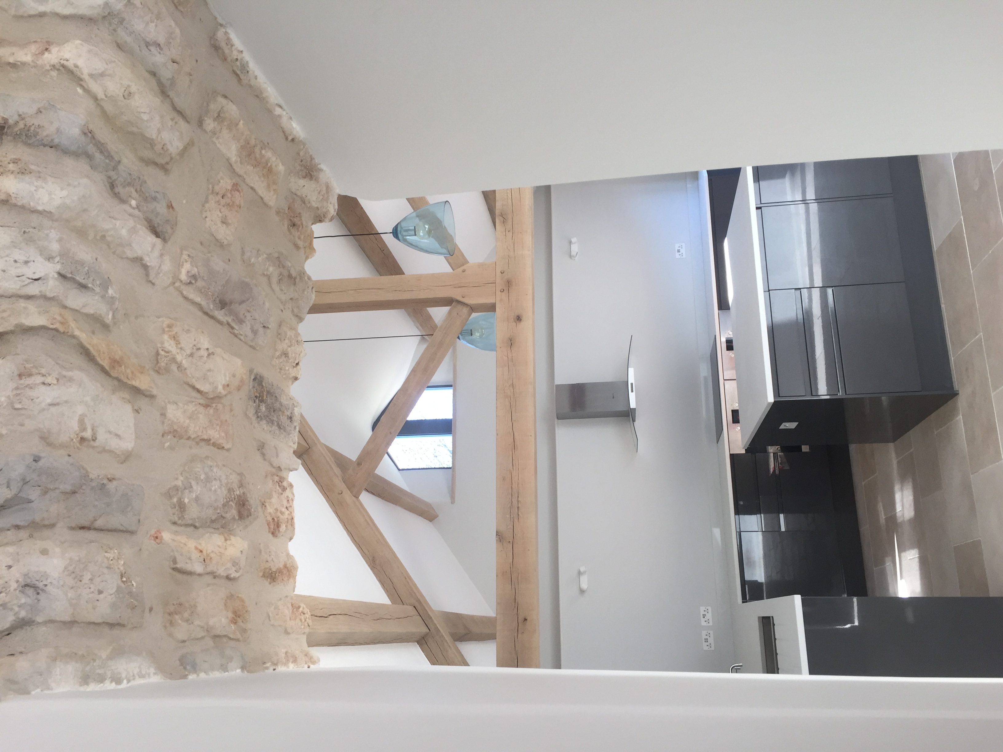 Open-plan kitchen beneath exposed stone and oak trusses with limestone flooring