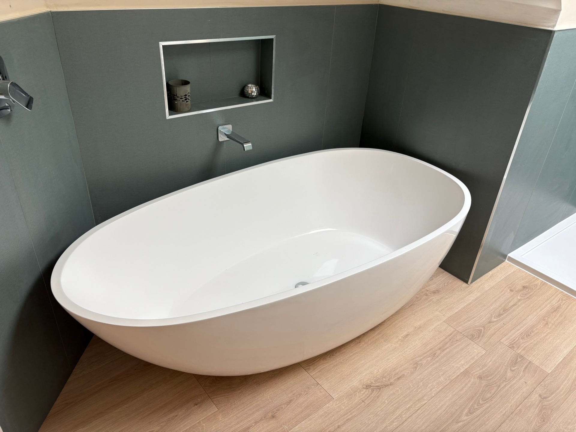 Freestanding oval bath against dark green tiled wall with recessed niche