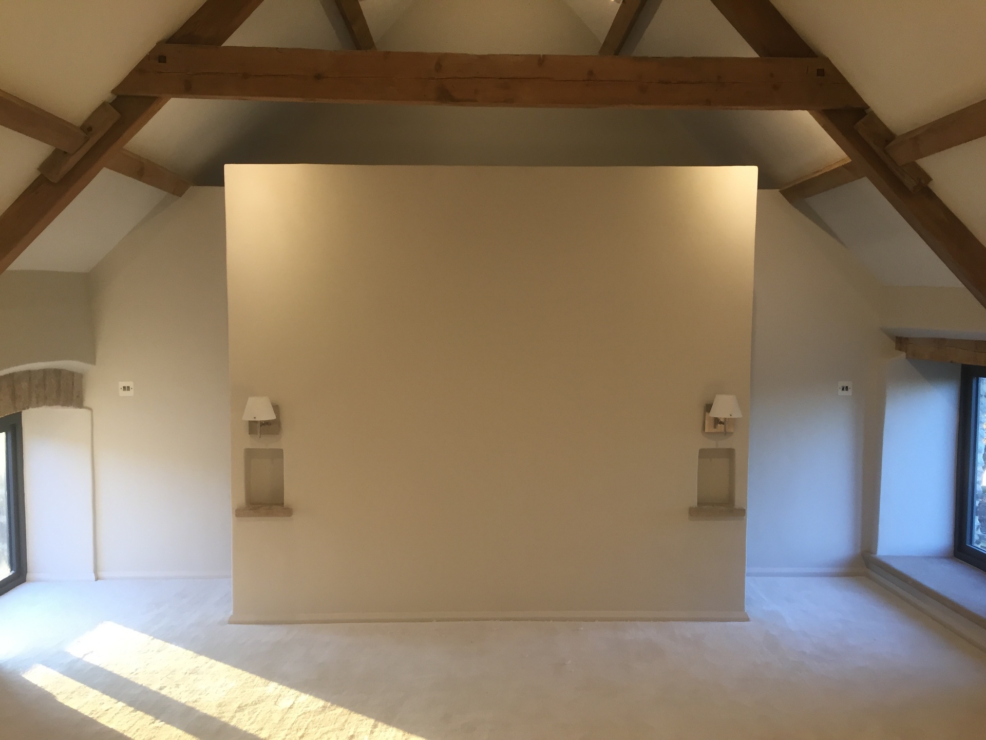 Bedroom with exposed oak roof trusses, sconce lighting and stone reveals
