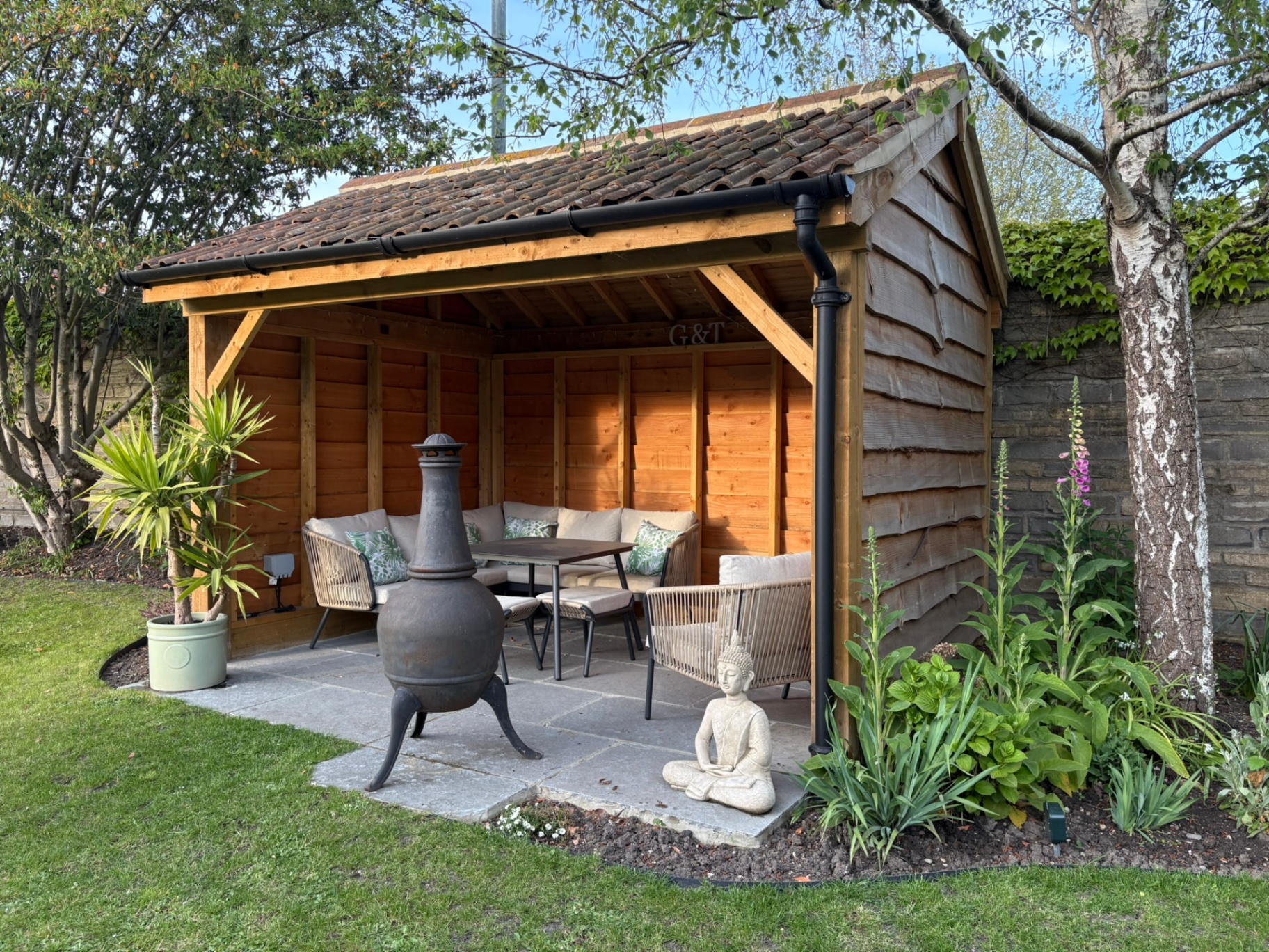 Oak-framed garden shelter with pantile roof, seating and planted borders