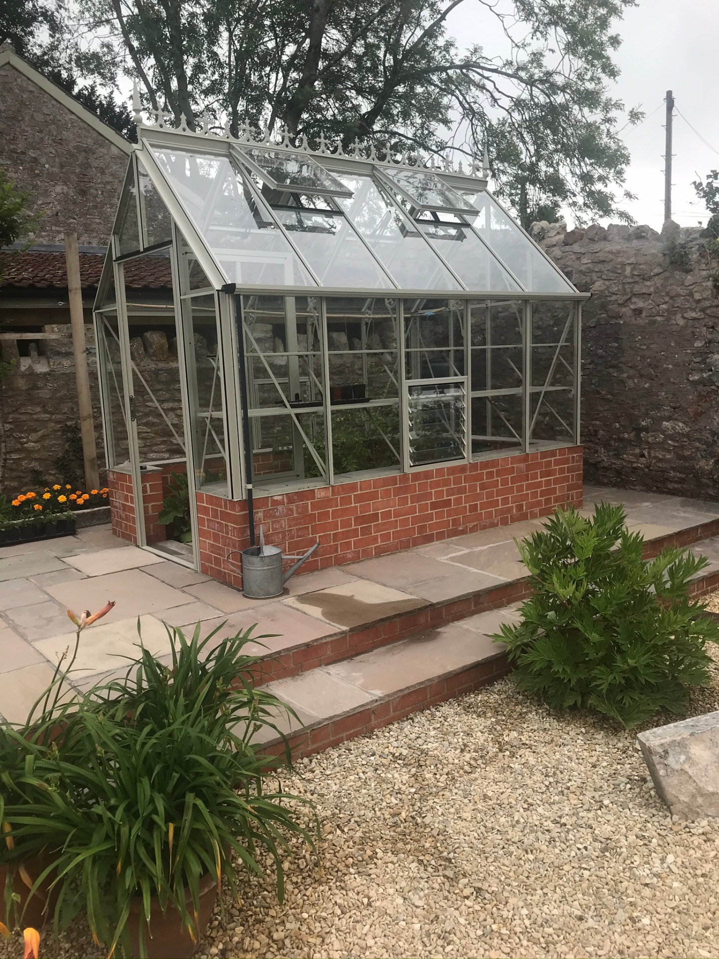 Victorian-style greenhouse on brick base with paved and gravelled surround