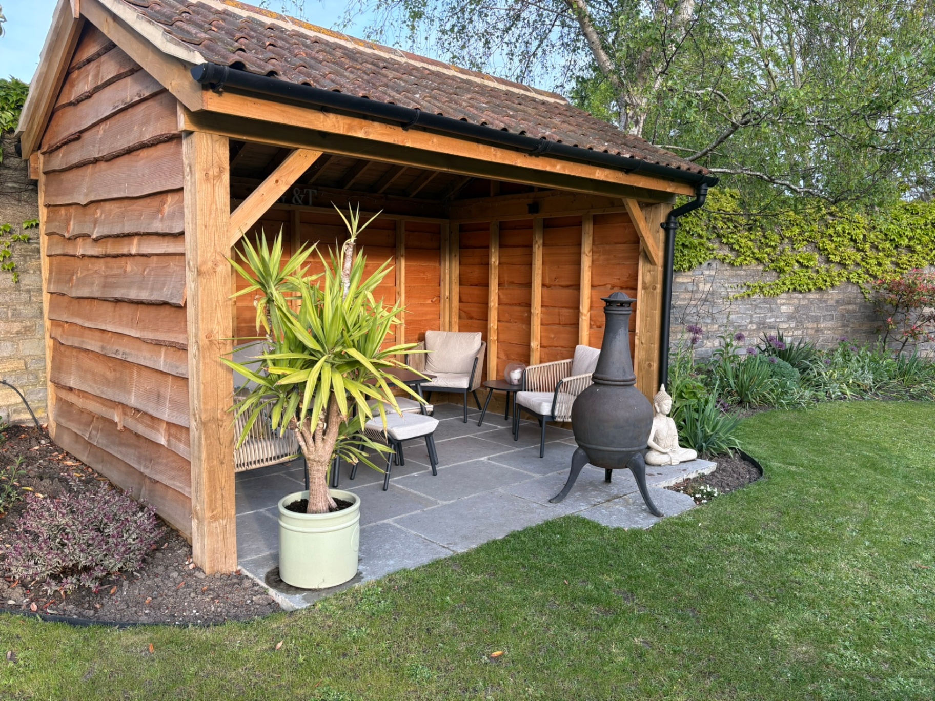 Side view of oak-clad garden shelter set into a landscaped garden