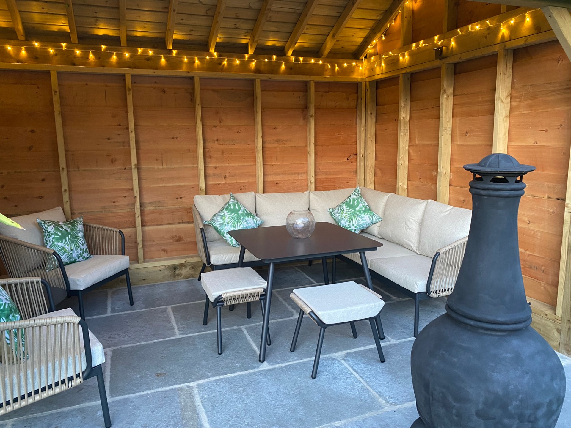 Covered outdoor seating area with corner sofa, dining table and chiminea