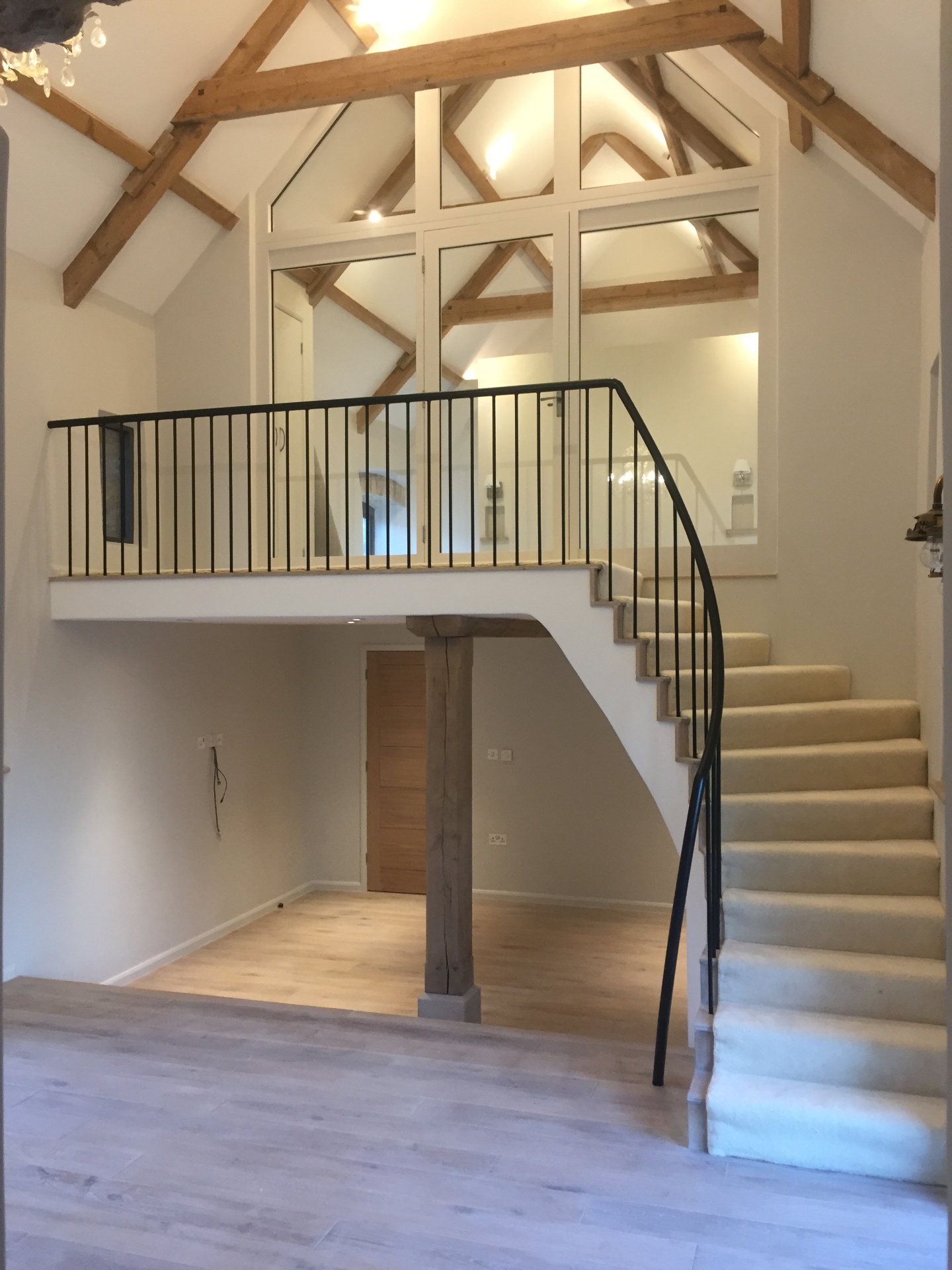 Double-height barn interior with exposed oak trusses, mezzanine and glass-panelled gable