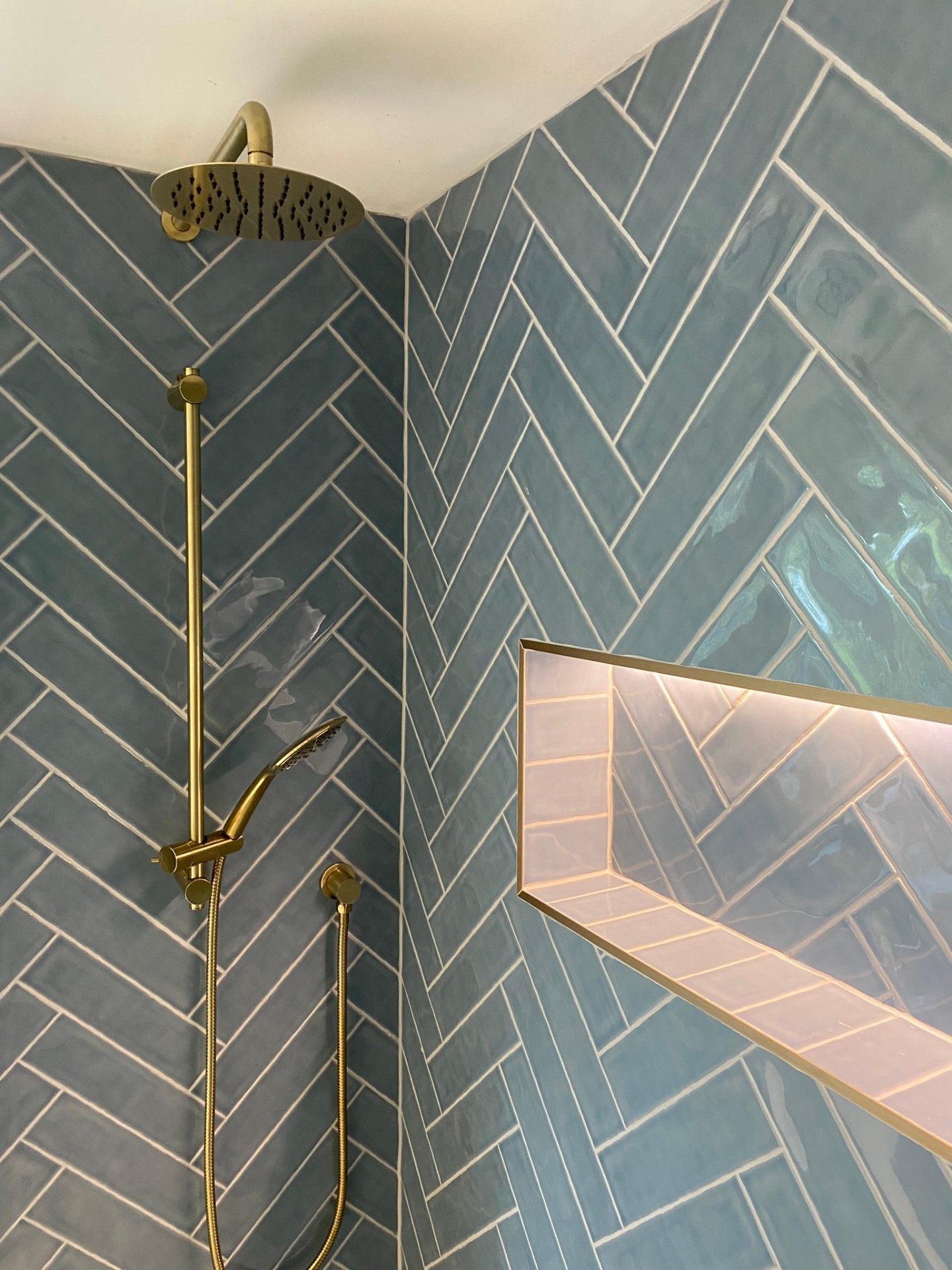 Teal herringbone shower detail with brushed brass rainfall and handset