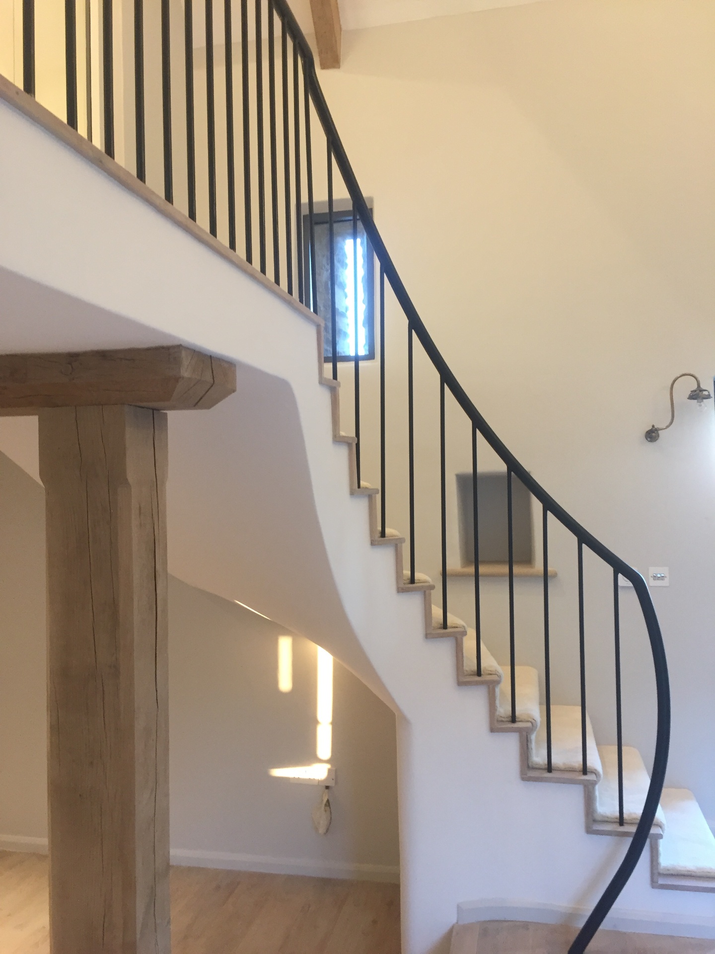 Curved plaster staircase with slim iron balustrade and oak newel post, lit by natural light