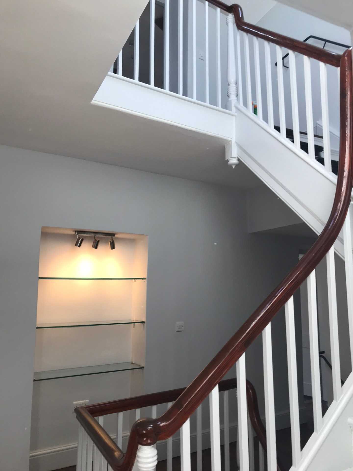 Painted timber staircase with polished mahogany handrail and glass-shelved display niche