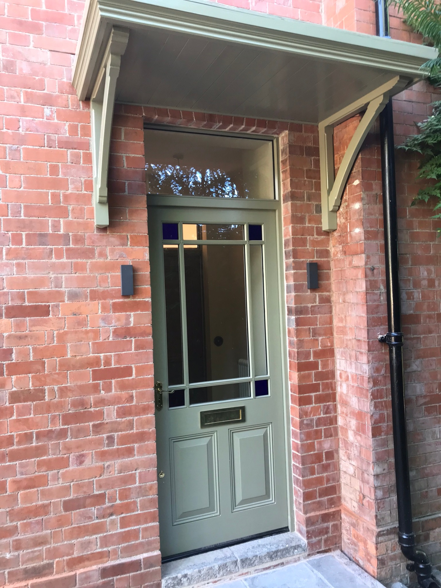 Restored front door with stained-glass panels beneath a bracketed porch canopy