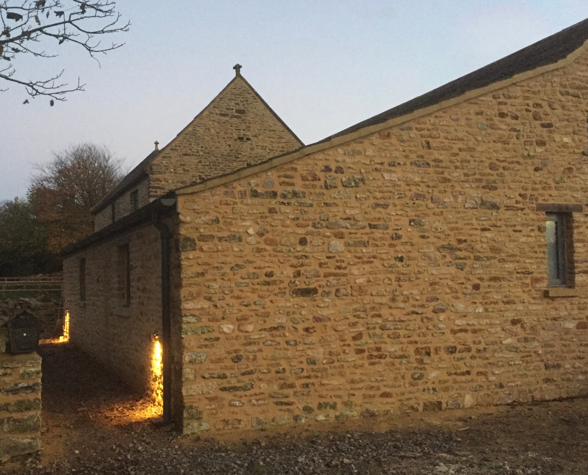 Rear elevation of the converted barn at twilight, showing the pitched roofs and repaired stonework