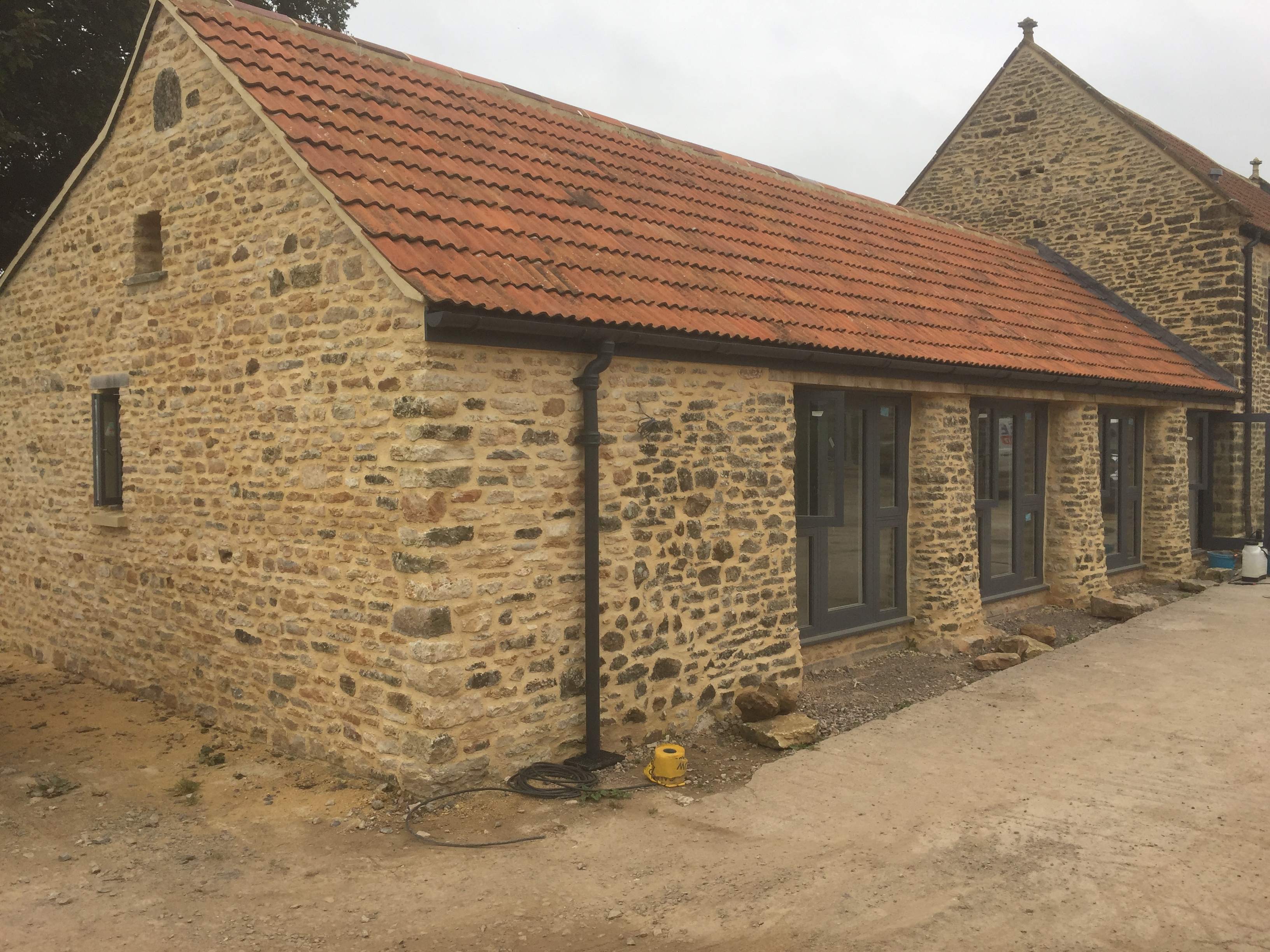 Exterior view of the converted listed barn with traditional stonework, clay tile roof and new grey-framed windows