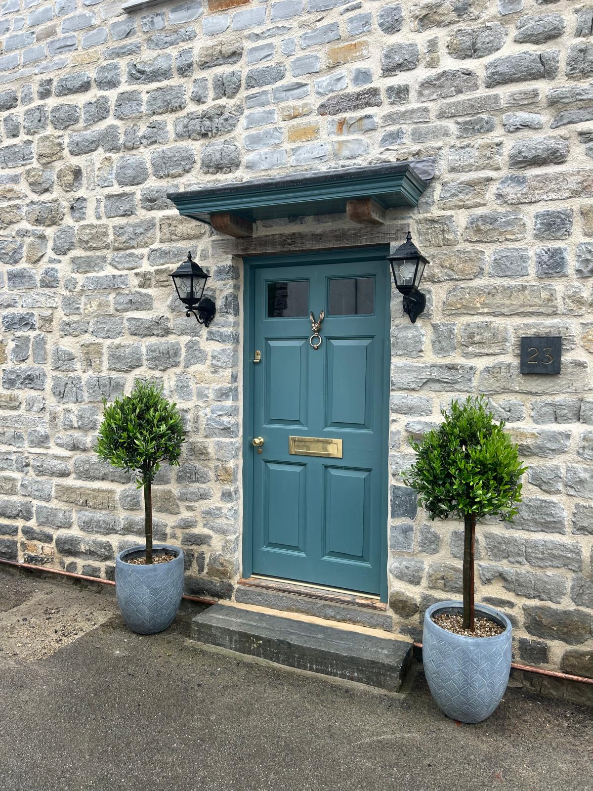 Traditional four-panel front door in heritage teal set within the stone façade